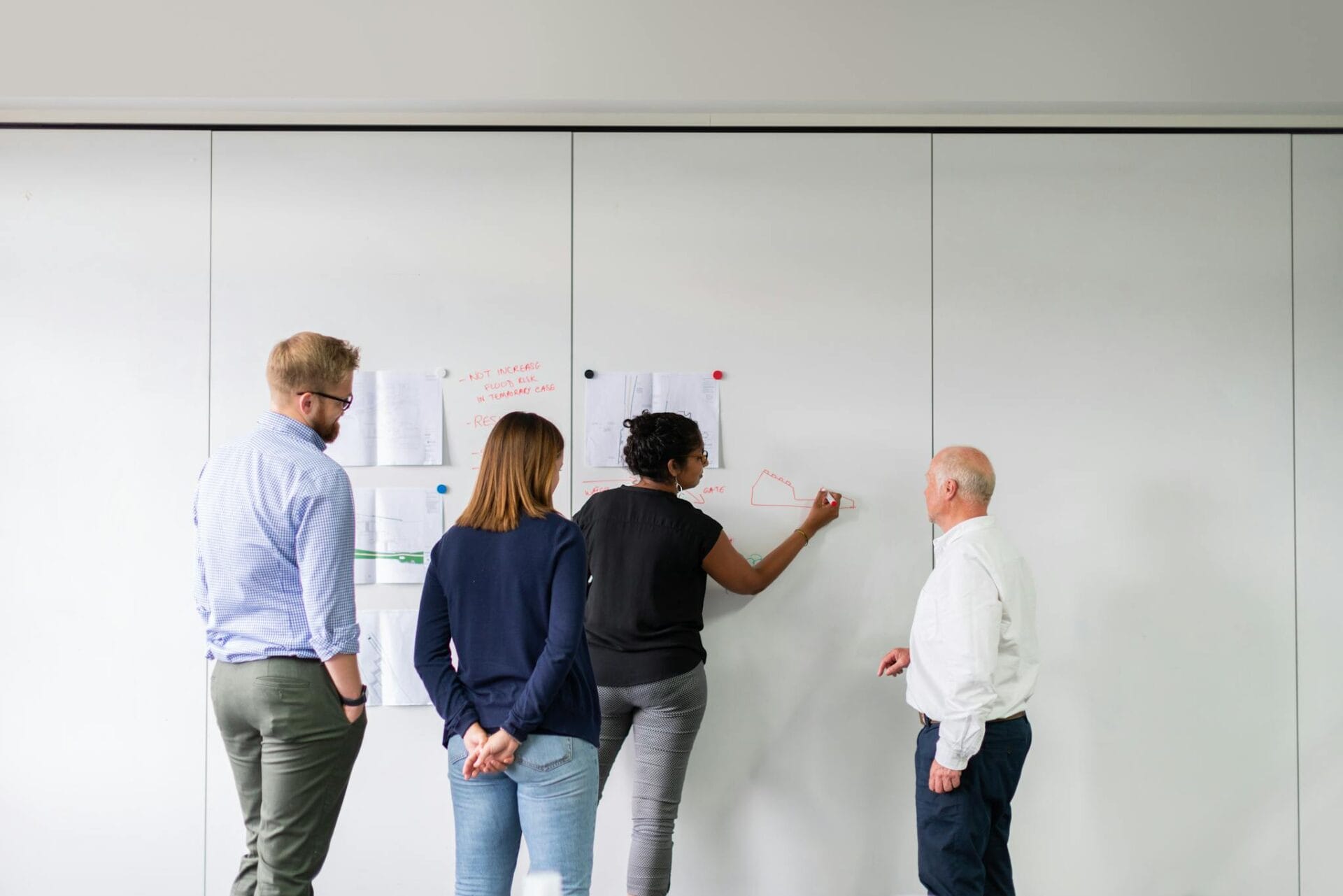 A diverse team of professionals engaged in strategic planning using a whiteboard in an office setting.
